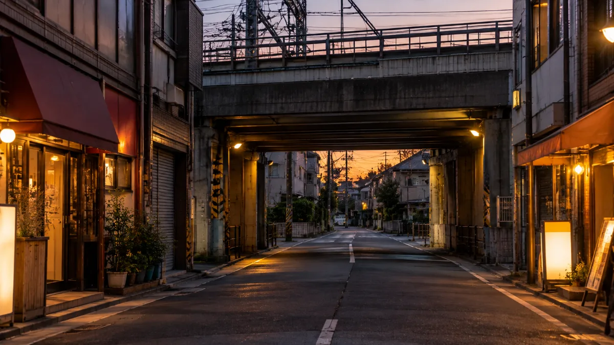 駅の高架をくぐる道。手前は商店が並ぶ通り、高架の向こうは住宅の静かな道に変わる